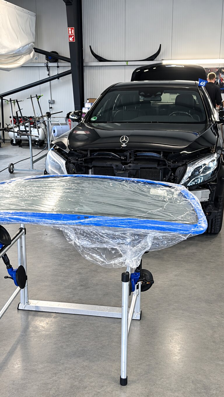 Mercedes in der Halle, davor eine eingepackte neue Frontscheibe auf dem Montageständer